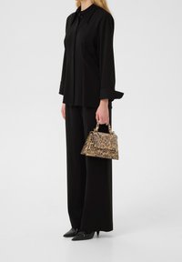 Chemise noire à manches longues, pantalon noir à jambes larges, et sac à main imprimé léopard avec une forme structurée et une poignée supérieure. Chaussures noires à bout pointu.