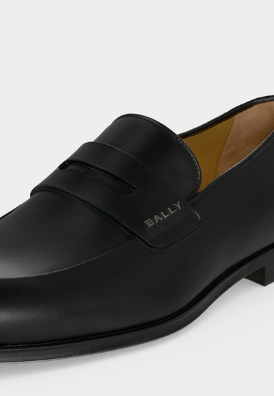 Μαύρο δερμάτινο επίσημο μοκασίνι με λουράκι που έχει κοπή και μεταλλικό λογότυπο "BALLY" στο πλάι.
