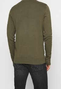 Maglione a maglia verde oliva con scollo rotondo, maniche lunghe e polsini e orlo a costine, abbinato a jeans in denim scuro.