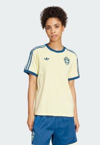 Žltý atletický dres s modrými akcentmi, s krátkymi rukávmi, okrúhlym výstrihom a so švédskym národným emblémom na hrudi.