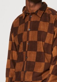 Chemise en flanelle à carreaux marron et beige avec un devant à boutons et un col. Présente une texture douce et une coupe standard.