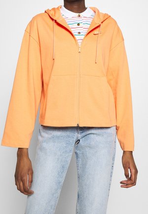 Sudadera con capucha de color naranja brillante, hecha de tela suave, con un bolsillo frontal y cordones, llevada sobre una camiseta de polo a rayas.