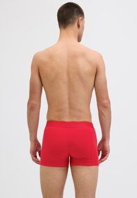 Rote Baumwoll-Boxershorts zeigen eine glatte Textur mit einer engen Passform und einem elastischen Bund, von hinten auf einem nackten Oberkörper dargestellt.