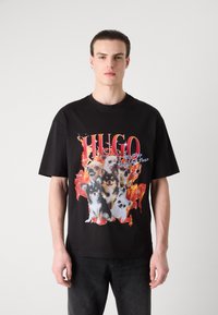 Černé bavlněné tričko s barevným grafickým vzorem z mnoha obrázků psů na pozadí plamenů. Velký nápis "HUGO" nahoře.