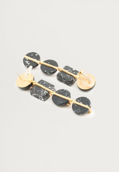 Orecchini in resina marmorizzata in bianco e nero con accenti in metallo dorato, caratterizzati da forme circolari e rettangolari su una barra di collegamento dorata.