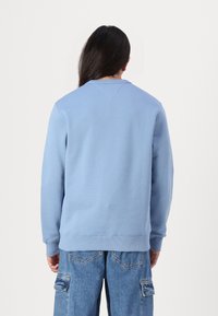 Felpa azzurra chiara con maniche lunghe, colletto rotondo e polsini a coste. Presenta un tessuto testurizzato e una vestibilità casual.
