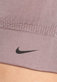 Gros plan sur un tissu athlétique côtelé mauve avec des coutures texturées et le logo Nike Swoosh noir sur la peau.