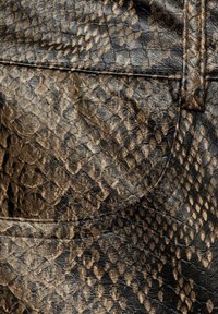 Gros plan d’un cuir synthétique à effet peau de serpent texturé brun foncé et noir avec des écailles détaillées et des coutures visibles.
