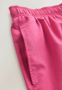 Shorts rose à coupe décontractée en tissu doux, avec une ceinture élastique et des poches latérales, présentant une texture lisse et des coutures nettes.