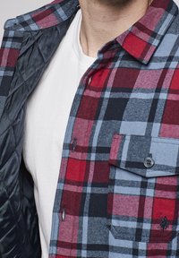 Rutig flanellskjorta i röd, blå och svart, med en kviltad marinblå foder, knäppbar krage och bröstficka med knapp.