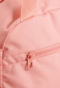 Borsa di tessuto rosa con superficie texturizzata, dotata di chiusura con zip e tiretto coordinato. Accentuata da una tracolla intrecciata.