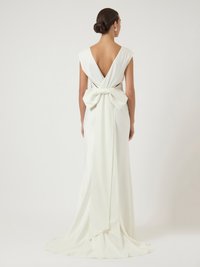 Λευκό φόρεμα με βαθύ V στην πλάτη και φαρδιά μανίκια. Διαθέτει μεγάλο φιόγκο στη μέση και μακρύ άλικο από ομαλό ύφασμα.