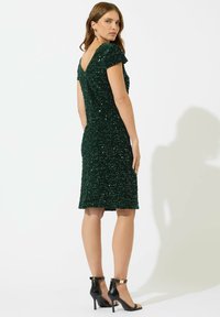 Abito verde con paillettes, design con scollo a V nel retro, maniche corte, taglio fino al ginocchio, abbinato a sandali neri con tacco alto. Texture liscia.