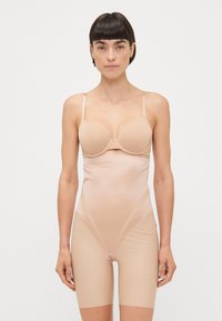 Nude shapewear med justerbare stropper, sømløst design og en tettsittende silhuett som strekker seg til midt på låret med en glatt tekstur.