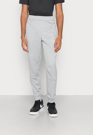 Person iført lysegrå joggebukser med "The North Face" logo på låret og sorte Nike-sneakers med hvide swooshes.