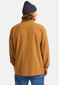 Brun, långärmad overshirt i strukturerad tyg, med klassisk krage och knapprör, bärs över blå denimjeans.