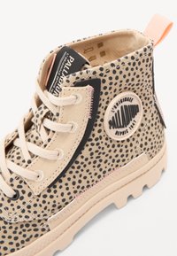 Botín de lona beige con lunares negros, costuras rosas, suela de goma, parche de logo y tirador. Presenta puntera redonda y diseño de cordones.