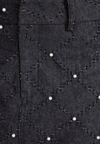 Svart denimstoff med en kviltet diamantmønster og små hvite perlepynt. Har en jevn tekstur og en subtil glans.