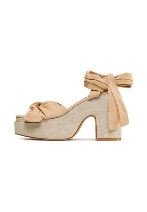 Beżowe buty na platformie z węzłową tkaniną na cholewce i wiązaniem wokół kostki, z teksturowaną podstawą przypominającą len oraz masywnym obcasem.