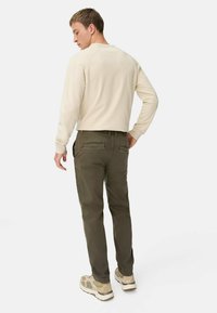 Cremefarvet pullover med rund hals, parret med mørkegrønne bukser med flade lommer, båret med beige sneakers på en ensfarvet baggrund.