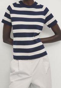 Navy and white striped knit shirt with a round neckline, short sleeves, and ribbed cuffs; paired with light, high-waisted trousers.