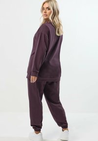 Lila Sweatshirt- und Jogginganzug aus weichem Stoff, mit elastischen Bündchen und Säumen für eine lockere Passform. Weiße Sneakers runden den Look ab.