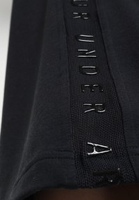 Black athletic shirt featuring a textured mesh panel with glossy lettering along the side, emphasizing breathability and style.