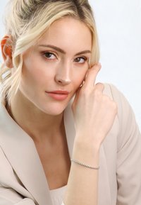 Silver bracelet with circular accents, worn on a light-skinned hand. Smooth texture against a soft, neutral-toned blazer.