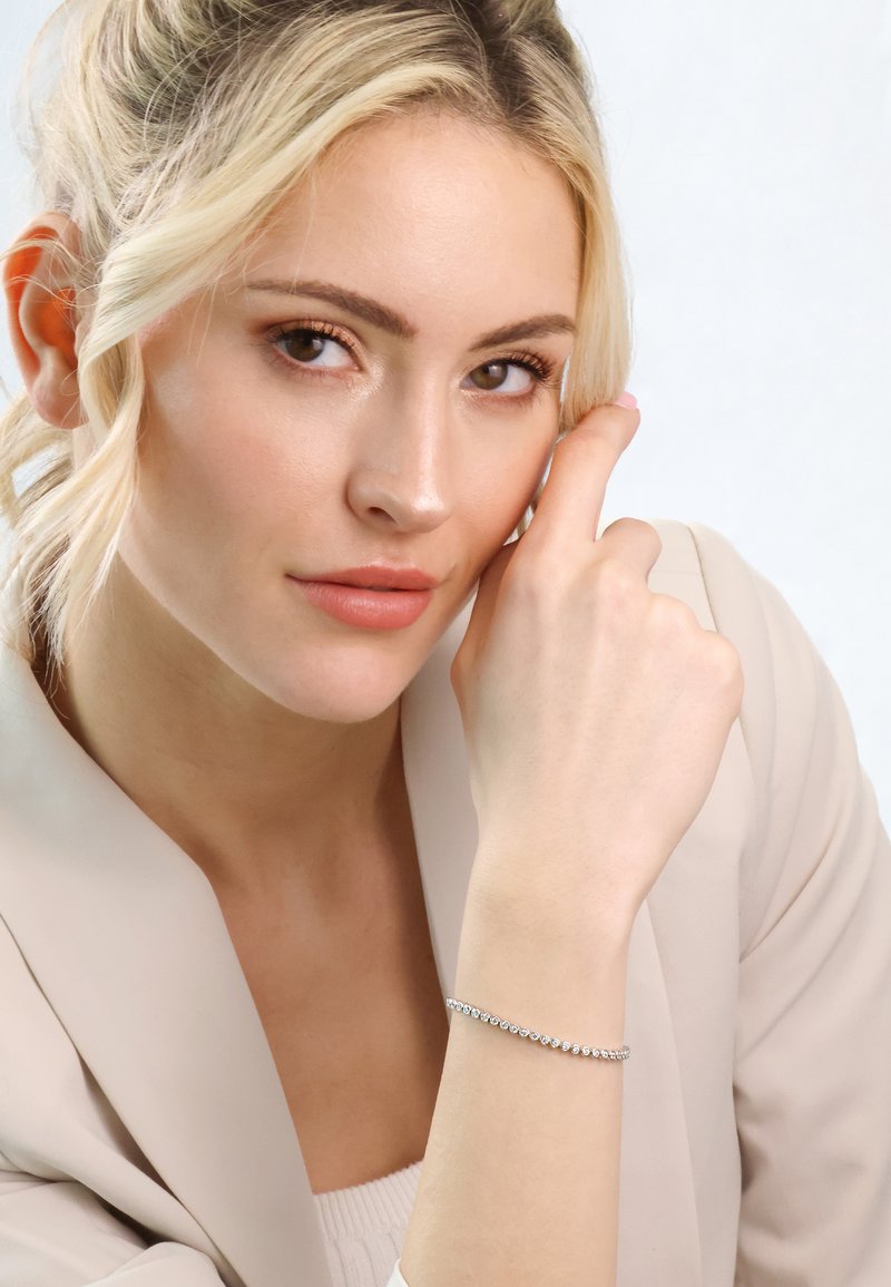 Silver bracelet with circular accents, worn on a light-skinned hand. Smooth texture against a soft, neutral-toned blazer.