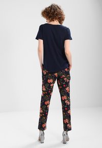 Námořnické tričko s krátkým rukávem v kombinaci s černými kalhotami s květinovým vzorem, které mají růžové a žluté květy. Modelka má na sobě stříbrné chunky podpatky.