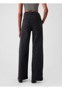 Jean taille haute et jambes larges en denim noir. Comprend deux poches arrière et un ourlet net. La texture semble robuste et lisse.