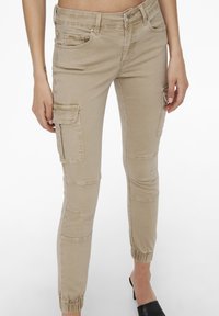Beige cargo pants with a slim fit, featuring patch pockets, elastic ankles, and a smooth fabric texture. No visible patterns or embellishments.