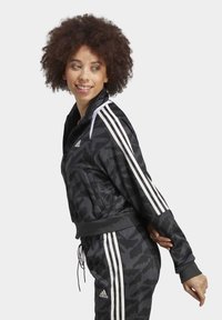 Black camo zip-up jacket with white stripes on sleeves and matching pants. Made from smooth fabric with ribbed cuffs and hem.