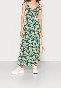 Maxiklänning i grön tyg med ett blommönster i rosa och krämfärgade blommor. V-ringad design och korta ärmar med en sidofåra.