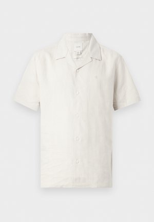 Biała lniana koszula z krótkim rękawem, zapinana na guziki, z klasycznym kołnierzem i subtelnym logo na piersi, pokazana na jednolitym tle.