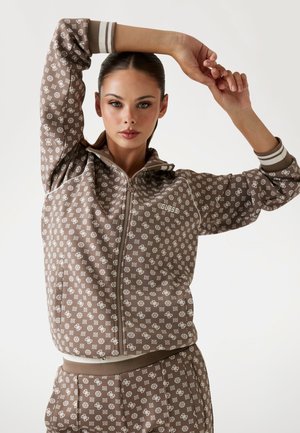 Brown zip-up hoodie with white patterned accents, featuring a hood, ribbed cuffs, and a matching design throughout.