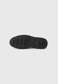 Suela de zapato de goma negra con ranuras y crestas horizontales. Textura lisa con un diseño de punta redondeada y tacón plano.