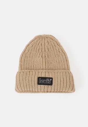 Berretto lavorato a maglia di color beige con texture a costine, caratterizzato da una toppa rettangolare nera sul fronte e un bordo ripiegato.