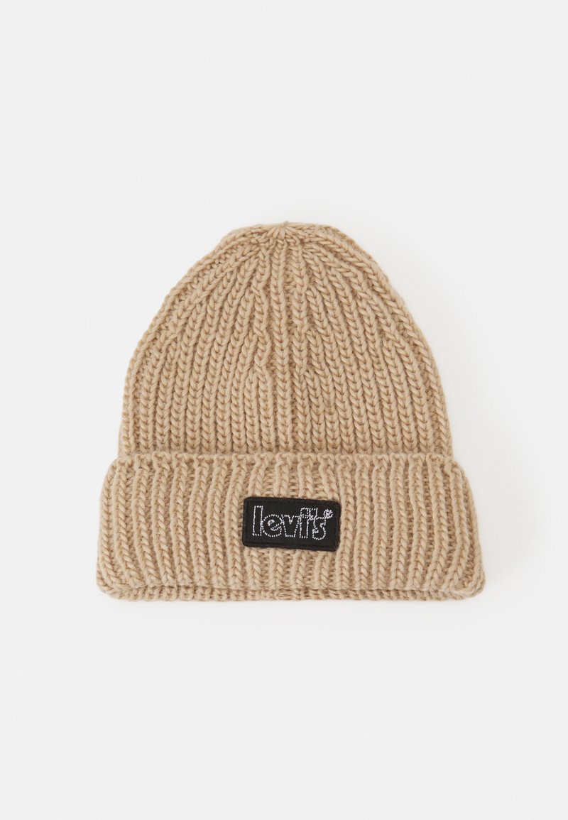 Berretto lavorato a maglia di color beige con texture a costine, caratterizzato da una toppa rettangolare nera sul fronte e un bordo ripiegato.