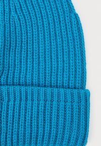 Lys blå strikket lue med ribbestruktur og brettet kant. Stoffet er mykt og har et jevnt mønster av hevede masker.