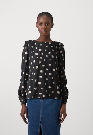 Black blouse with beige abstract square pattern, elasticized cuffs, round neckline, and slightly puffed sleeves paired with a denim skirt.