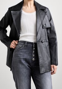 Musta nahkatakki leveällä kauluksella, kaksirivisillä napilla ja olkasaumoisilla yksityiskohdilla. Yhdistetty korkeavyötäröisten tummien denim-farkkujen kanssa, joissa on koristeellisia nappeja.