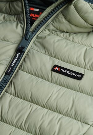 Lys grøn isoleret jakke med quiltet tekstur, med en mørk lynlås og Superdry-logo på lappen. Lynlåsdetaljer langs forsiden.