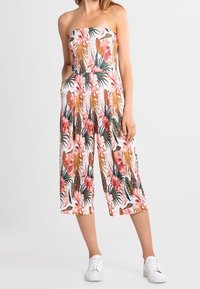 Combinaison florale sans bretelles, avec des motifs tropicaux roses et verts, jambes larges et courtes, et deux poches latérales.