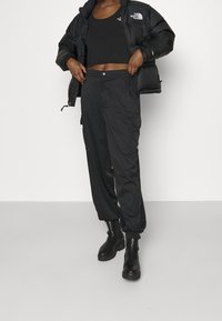 Chaqueta de plumón negra con diseño recortado, combinada con pantalones cargo negros de corte holgado que cuentan con bolsillos y puños en el tobillo, completado con botas negras.