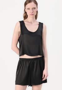 Svart sateng cropped topp med bred hals og ermeløs design, kombinert med matchende høytosede shorts med elastisk linning.