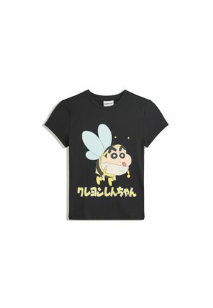 T-shirt en coton noir avec un personnage de dessin animé aux accents jaunes et bleus, texte en japonais sous le graphique. Manches courtes, col rond.