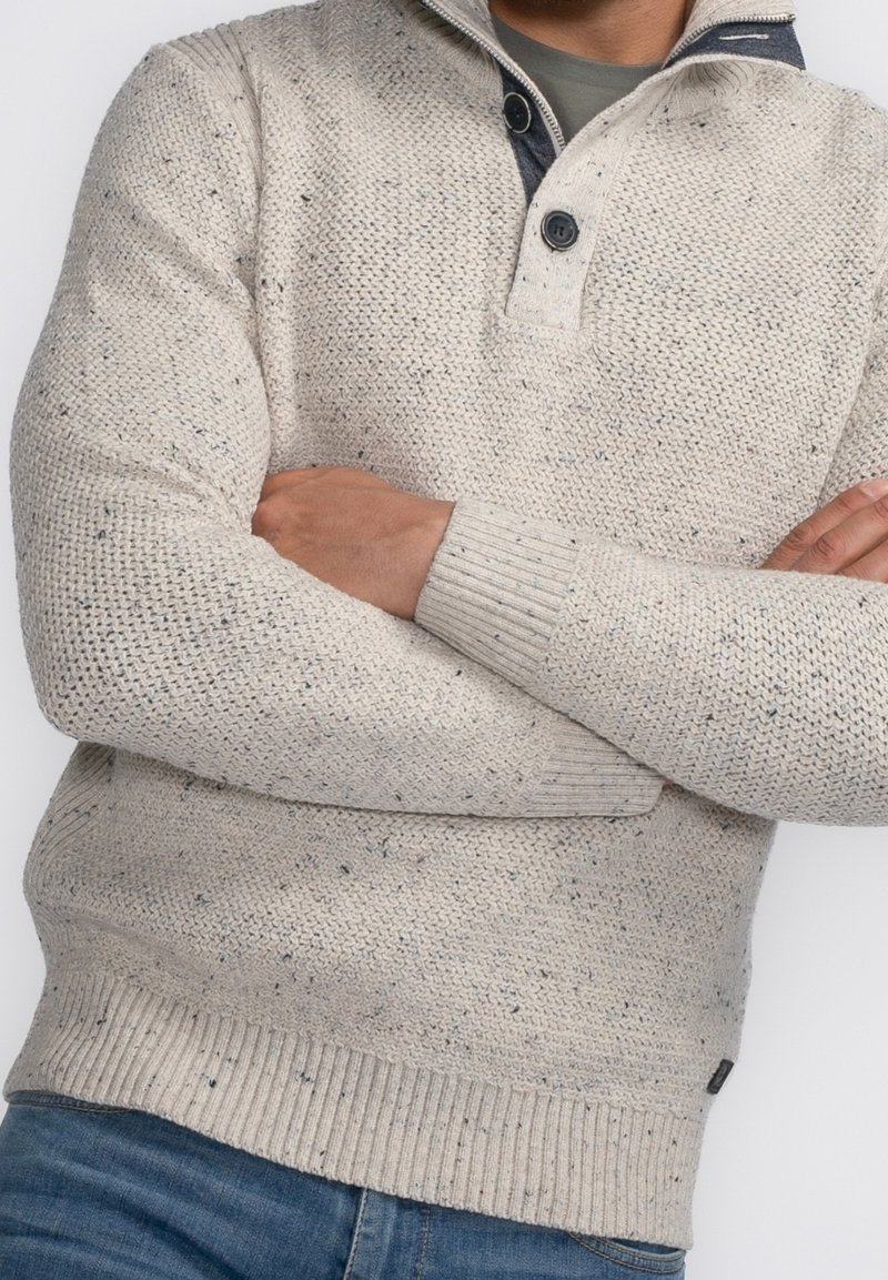 Pull tricoté beige clair avec un col, doté de deux boutons, tissu texturé, et poignets et ourlet côtelés. Équipé d'un motif discret moucheté.