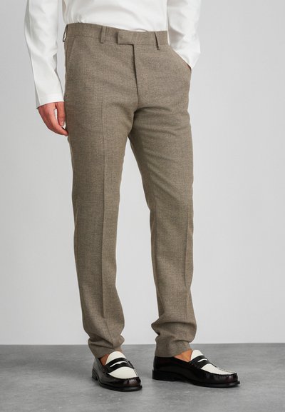 Pantaloni marroni a fantasia con taglio dritto, caratterizzati da pince frontali e una texture liscia. Abbinati a mocassini bianchi e neri.
