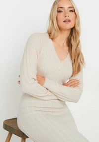 Beiges geripptes Strickkleid mit V-Ausschnitt, langen Ärmeln und figurbetontem Schnitt, das eine weiche Textur und subtile vertikale Linien aufweist.